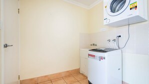 Een wasserette met een voorlader wasmachine, een droger, een betegelde vloer en een deur.