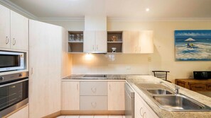 A modern kitchen with built-in appliances, a double sink, and a painting of a beach scene.