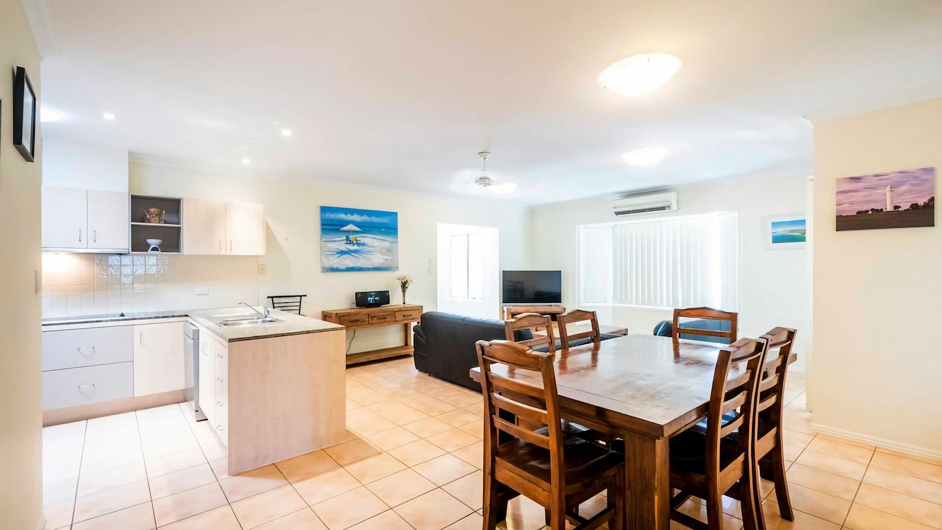 Una cocina moderna con una isla central, un comedor con sillas de madera y una sala de estar con sofá y televisión.