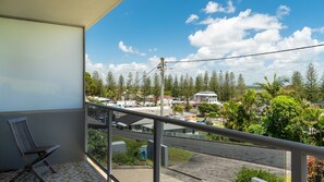 A balcony with a view of a residential area, a street, and a building with a white roof.