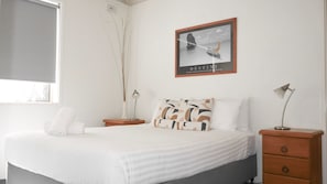 A neatly arranged hotel room with a bed, bedside tables, a lamp, a framed picture on the wall, and a window with a view. - Yamba Towers 2- Stone Real Estate Yamba (Yamba)
