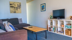 Un soggiorno con un divano, un tavolino, una televisione su un mobile basso e una libreria con libri e oggetti decorativi.