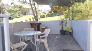 An outdoor patio with a table and chairs, a wooden bench, and potted plants. - Yamba Towers 2- Stone Real Estate Yamba (Yamba)