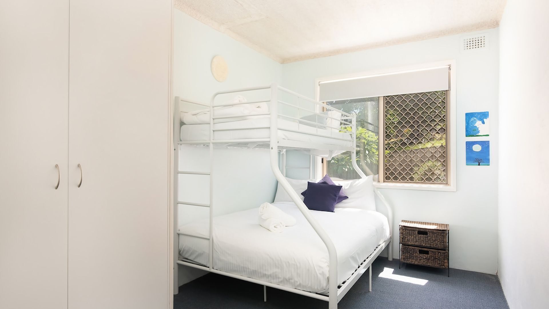 Een slaapkamer met een stapelbed, een raam, een tafeltje en een mand.