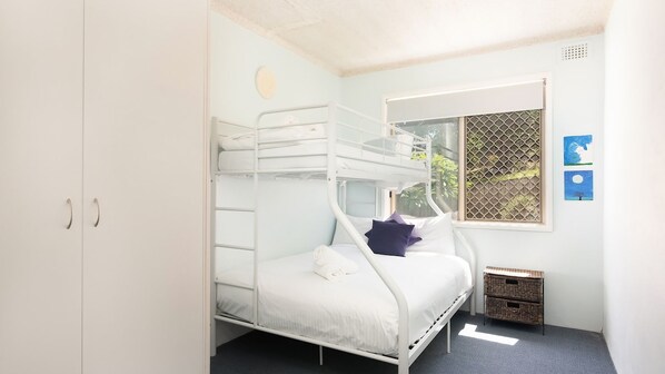 A bunk bed room with a window, a small table, and a basket.