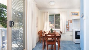 A dining area with a table and chairs, a kitchen with a stove, and a window with curtains.