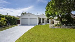 A two-story house with a garage, a well-maintained lawn, and a stone wall. - Kailani Beach House - Stone Real Estate Yamba (Yamba)