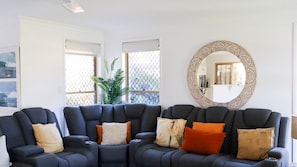 Una sala moderna con un sofá modular, un espejo decorativo y vistas a través de una ventana con una planta.