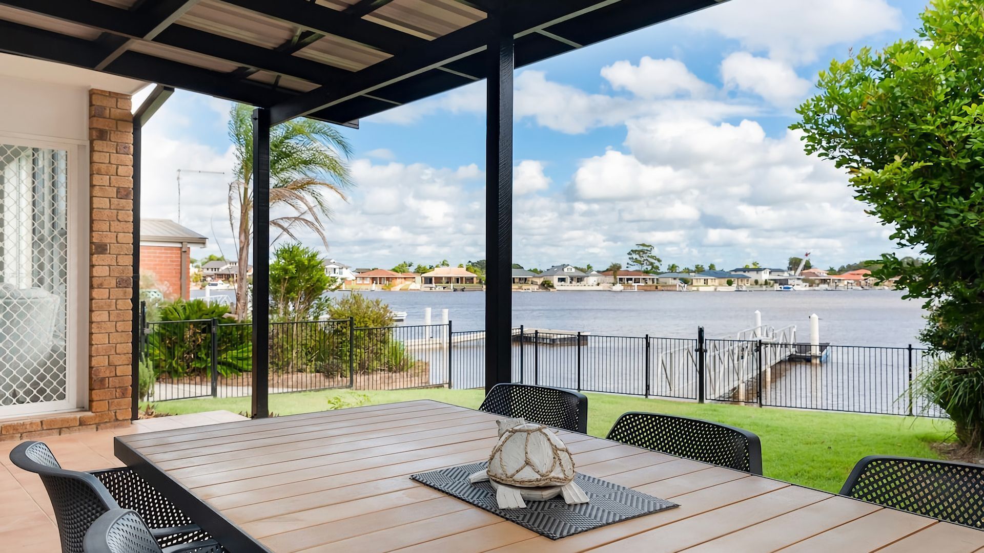 A covered outdoor dining area with a view of a body of water and houses in the background.