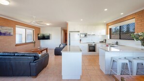 A modern kitchen with white cabinets, a central island, and a dining area with a black leather sofa.