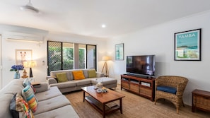 Una sala de estar con sofá, mesa de centro, televisor, sillón de mimbre y obras de arte.