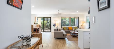 A modern living room with a sofa, coffee table, and dining area with wicker furniture.