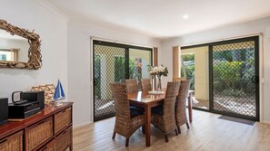 A dining area with a table set for four, surrounded by wicker chairs, a wooden cabinet with a television, and a decorative sailboat. - 32 Beachside Way -Stone Real Estate Yamba (Yamba)