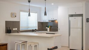 A modern kitchen with a central island, white cabinetry, a built-in oven, and a refrigerator.