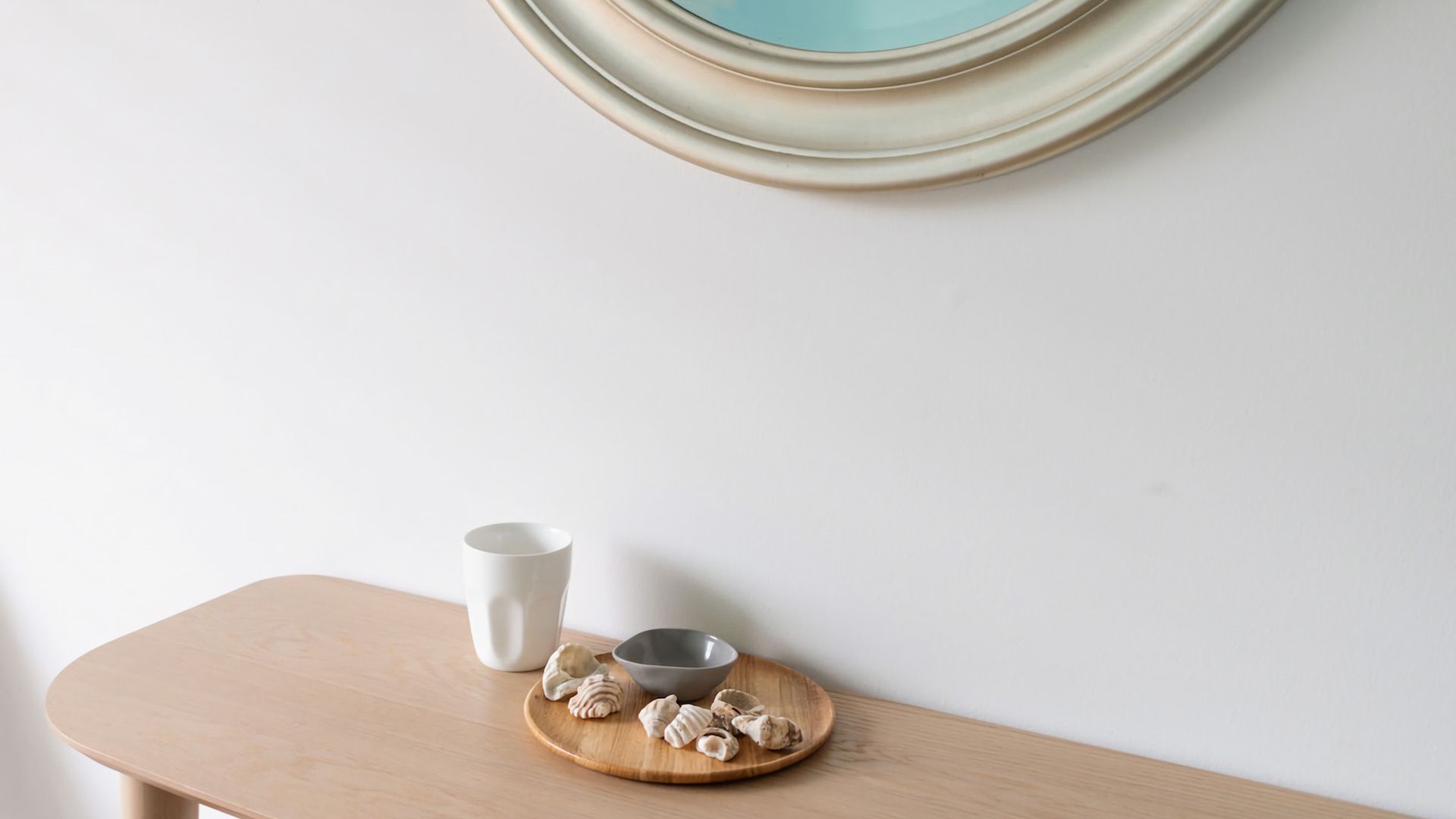 A table with a white mug and a gray bowl on a wooden tray, a white wall, and a decorative plate in the background.