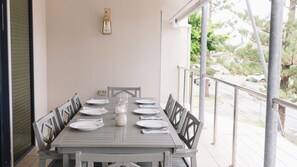 Une table à manger dressée pour six personnes, avec des chaises, un luminaire au-dessus et une vue sur la verdure à l’extérieur.