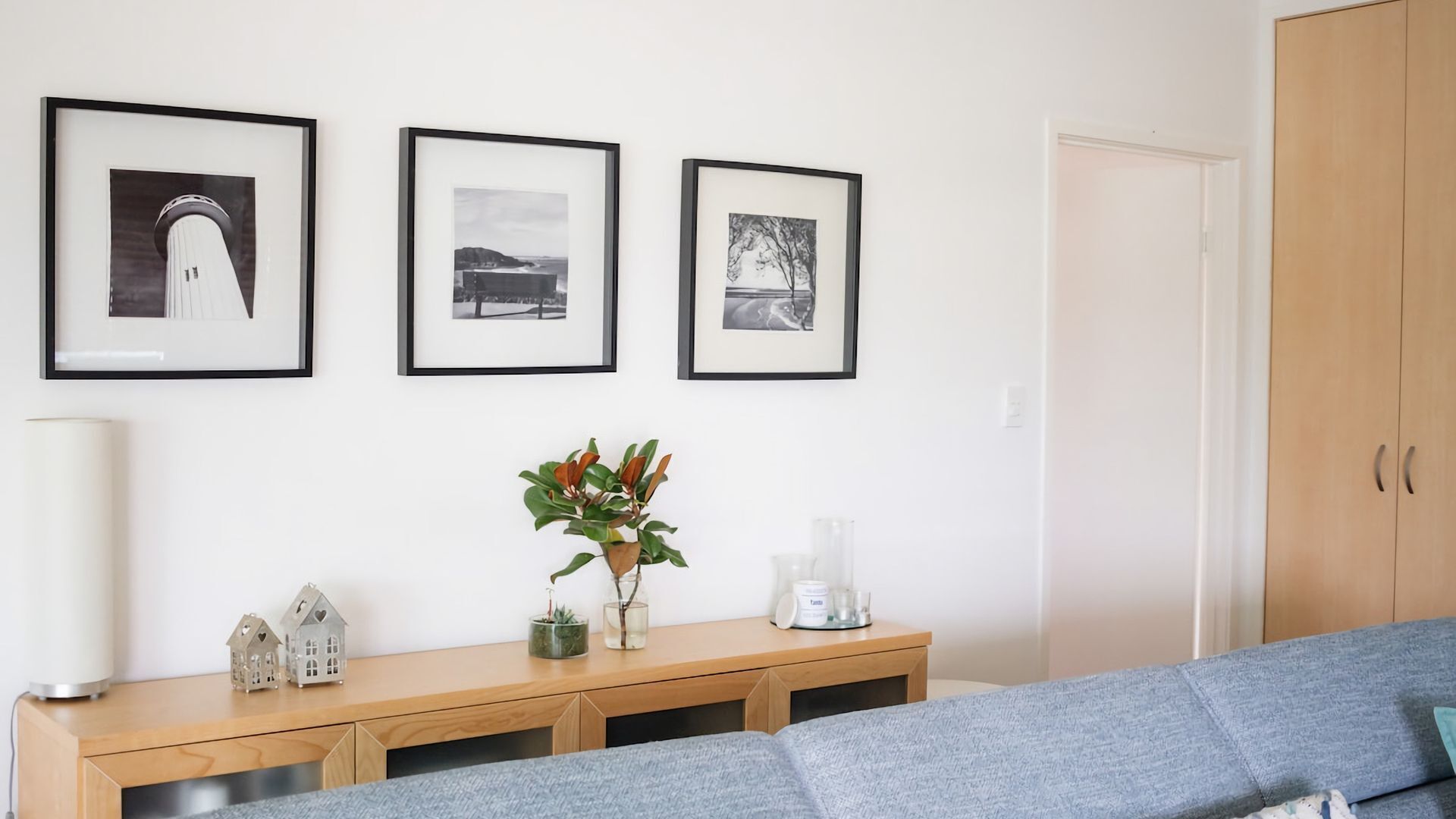 Ein modernes Wohnzimmer mit einem grauen Sofa, einem Holzkonsole und dekorativen Accessoires sowie drei gerahmten Bildern an der Wand.