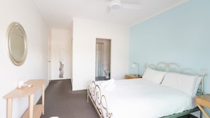 Een hotelkamer met een bed, nachtkastje, bureau, spiegel en een deur naar een badkamer.