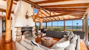 A spacious living room with a fireplace, large windows, and a view of the outdoors. - Casa Del Rio- Stone Real Estate Yamba (Ashby Heights)