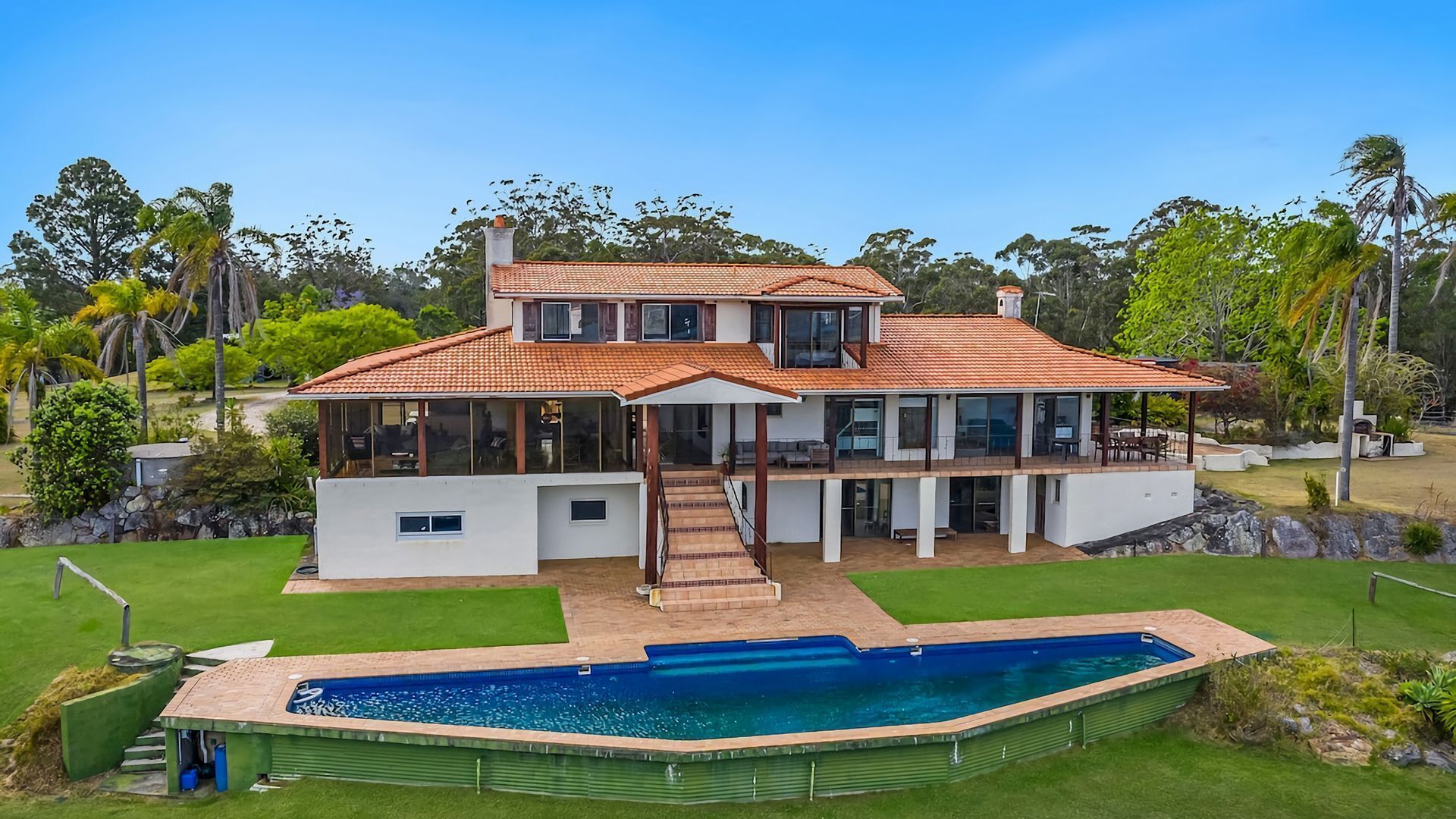 A two-story house with a large front yard, a swimming pool, and a covered outdoor area.