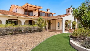 A Mediterranean-style house with a paved driveway, a covered patio, and a well-maintained lawn.