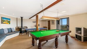 A room with a pool table, sofa, and a television.
