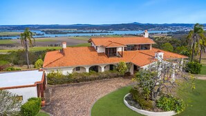 A two-story house with a red-tiled roof, a covered patio, and a view of a lake and hills in the distance.