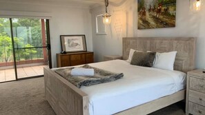 A bedroom with a large bed, a nightstand, a dresser, a framed picture, and a painting on the wall. - Casa Del Rio- Stone Real Estate Yamba (Ashby Heights)