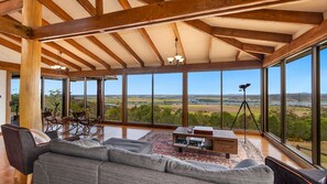 A spacious room with a large window, a sofa, a coffee table, and a tripod with a camera.