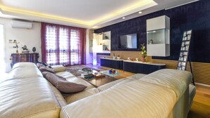 A modern living room with a large sofa, a coffee table, and a TV mounted on the wall.