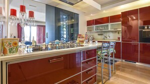A modern kitchen with red cabinetry, a central island with a sink, and a chandelier.