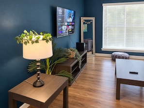 A living room with a TV, a lamp, a sofa, and a window with blinds.