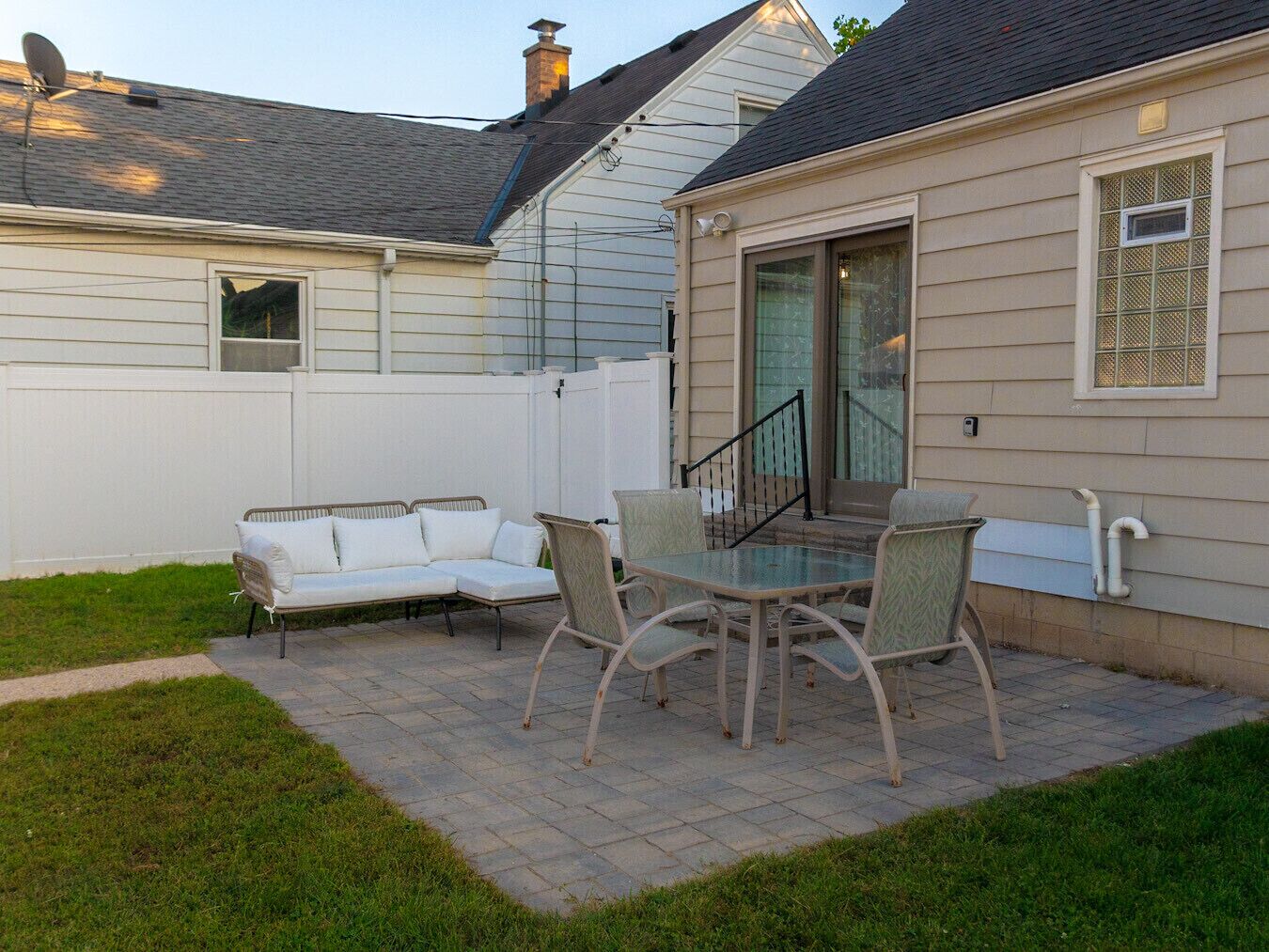 A patio with a glass table and chairs, a white sofa, and a white fence.
