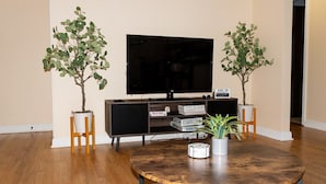 Un salon équipé d’un téléviseur à écran plat, de deux plantes en pot, d’une table basse ronde et d’une bibliothèque remplie de livres.
