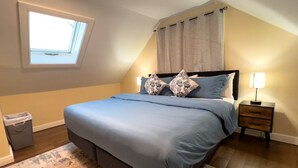 Une chambre à coucher avec un lit, une table de chevet, une lampe, une fenêtre et un rideau.