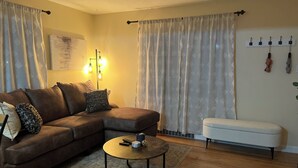 Un salon avec un canapé d’angle marron, une table basse ronde, un pouf blanc et un tapis à motifs.