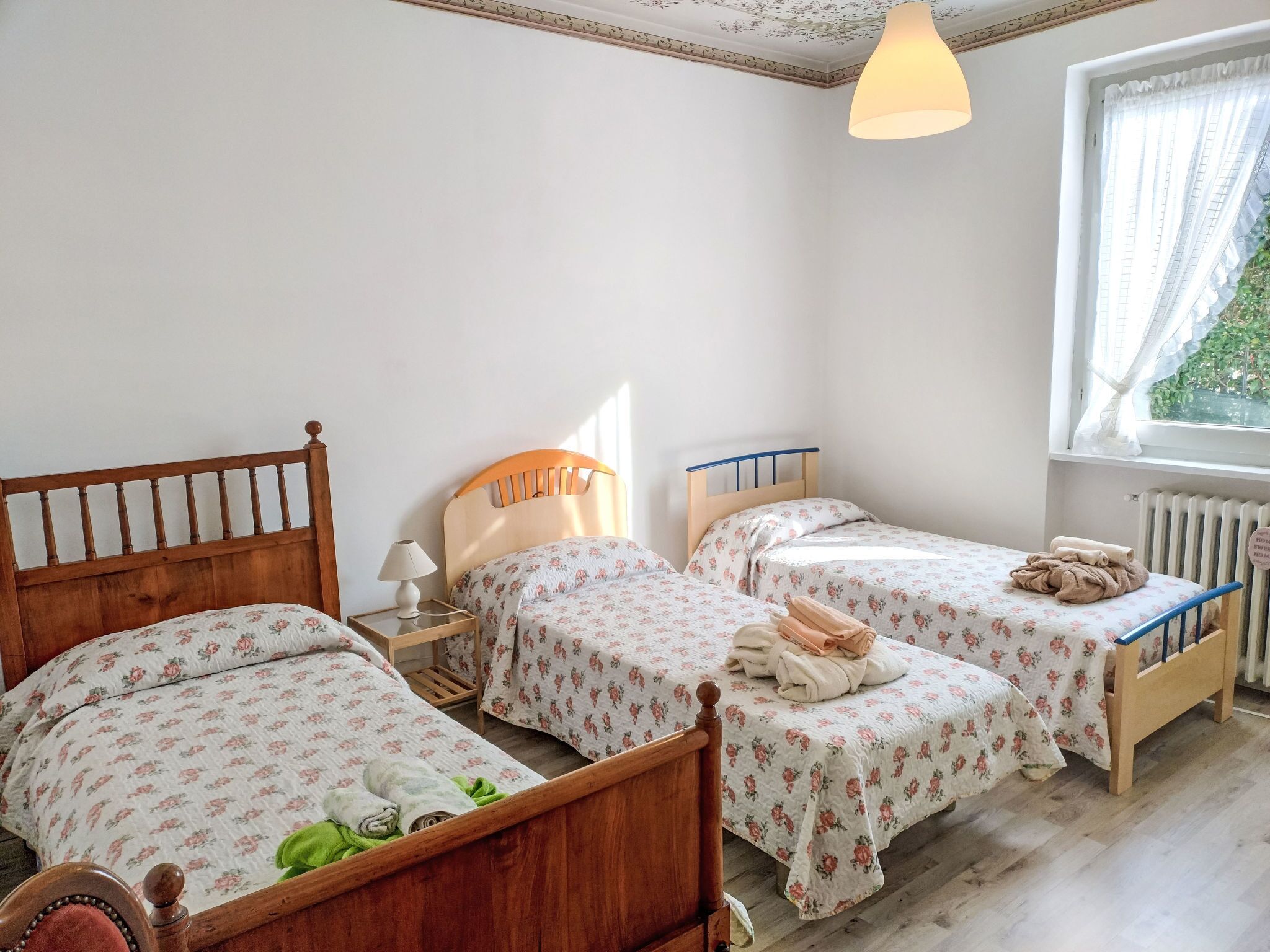 Un dormitorio con dos camas de madera, una mesita de noche con lámpara, un radiador y una ventana con cortinas.