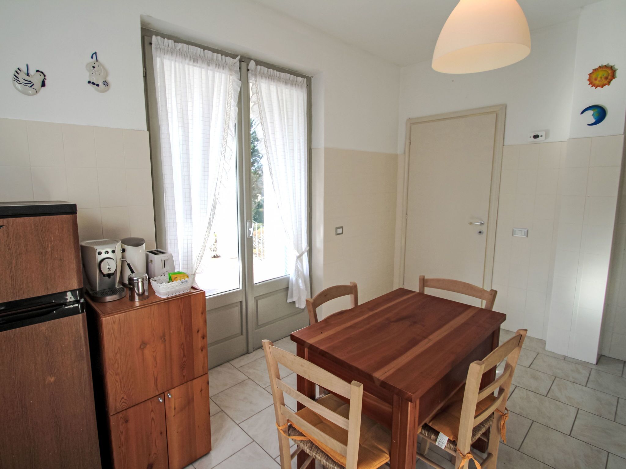 A small kitchen with a wooden table and chairs, a coffee maker, and a refrigerator.
