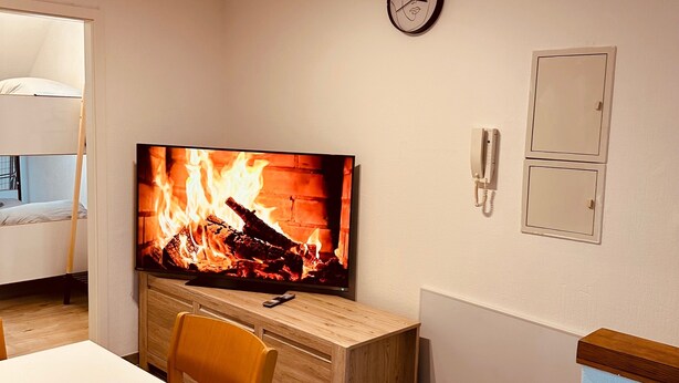 Ein Zimmer mit Fernseher, der einen Kamin zeigt, einer Uhr, einem Telefon und einem Schreibtisch mit Stuhl.
