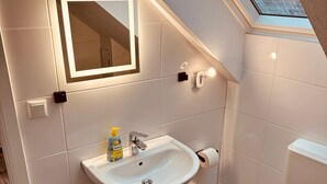 Ein modernes Badezimmer mit Oberlicht, einem weißen Waschbecken, einem Spiegel und einer Toilette.
