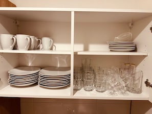 Une cuisine avec des étagères blanches où sont rangées des assiettes, des tasses et de la verrerie.