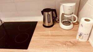 Eine Küche mit einer schwarzen Induktionskochplatte, einem Edelstahl-Wasserkocher, einer weißen Kaffeemaschine und einer Rolle Küchenpapier.