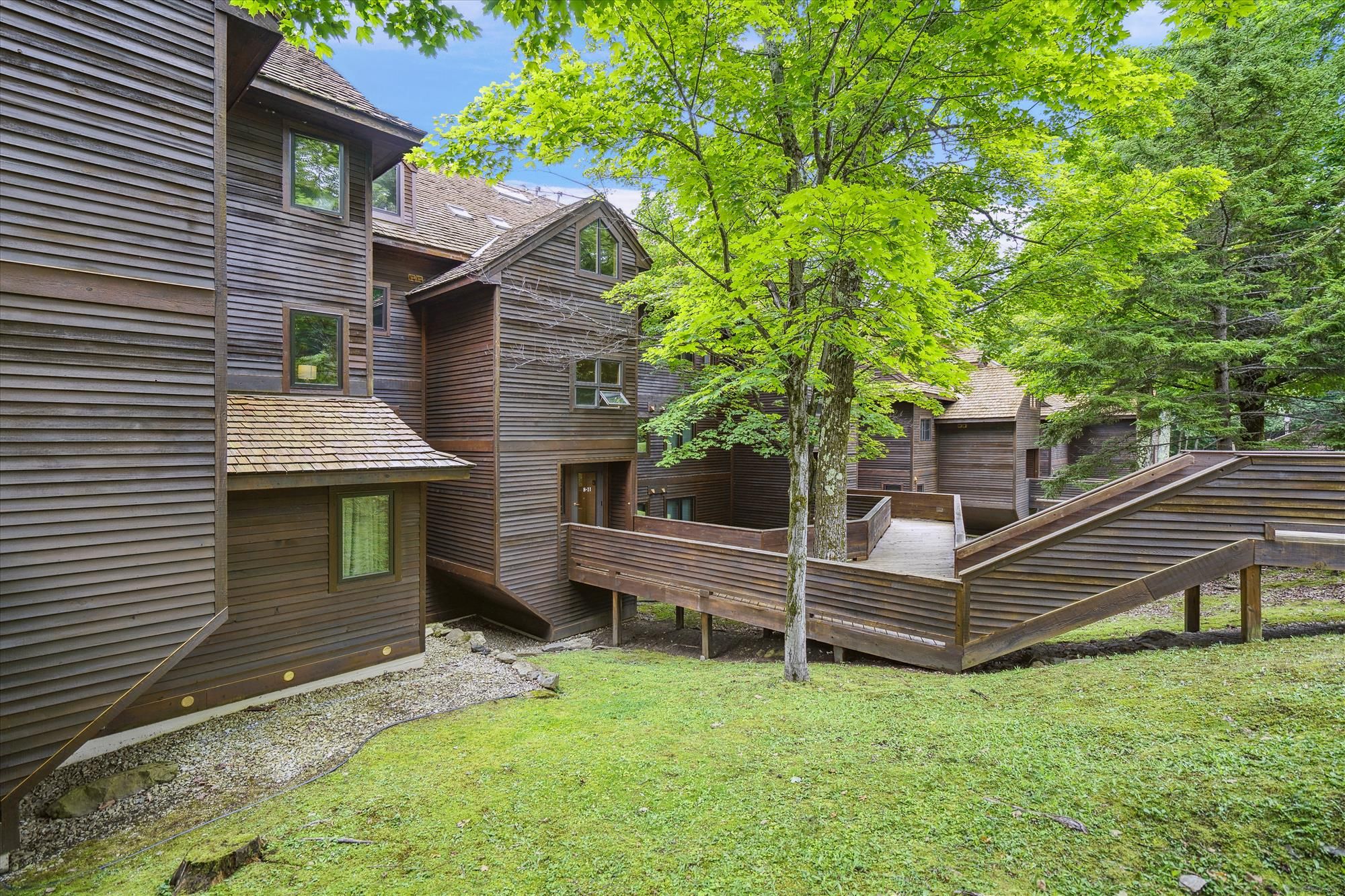 Une cabane en bois avec un toit en pente, une petite terrasse et un arbre au premier plan.
