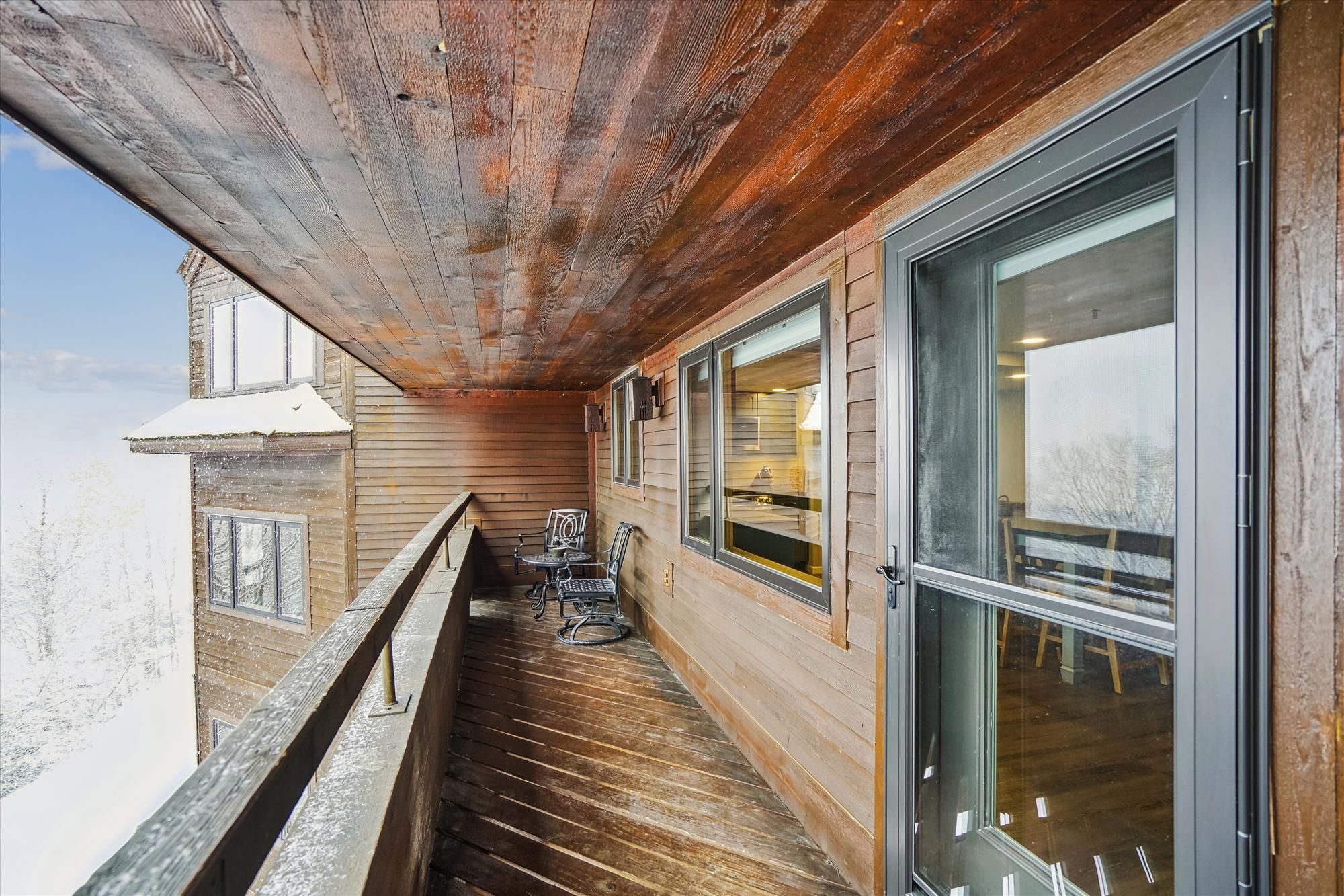 Un couloir extérieur en bois, doté d’un balcon, de grandes fenêtres et offrant une vue sur l’extérieur.