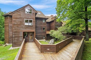 Une maison moderne en bois, dotée d’un toit en pente, d’un porche et d’un jardin aménagé avec une terrasse en bois.