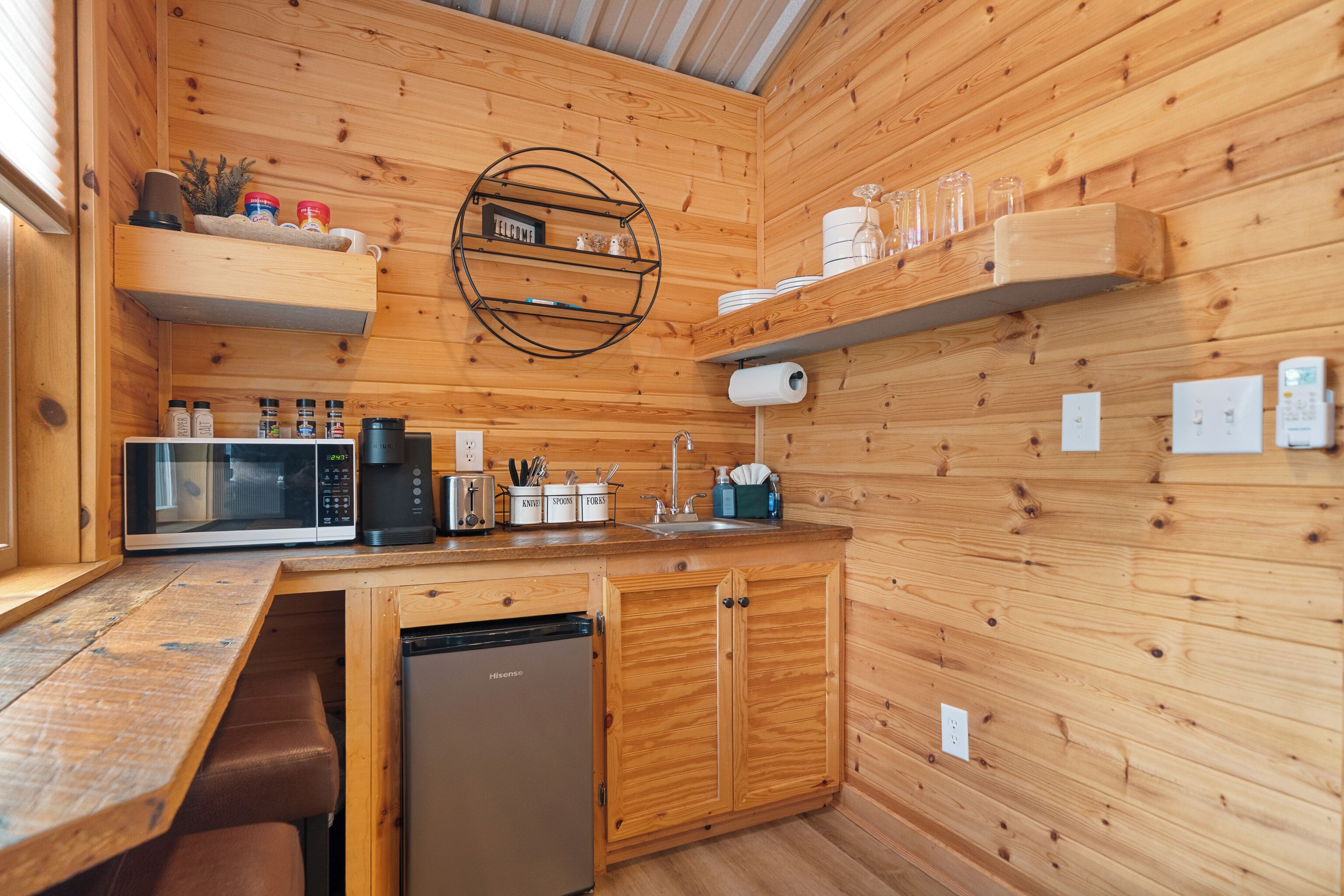 Een compacte keuken met houten wanden, een ingebouwde magnetron, een spoelbak en een vaatwasser.