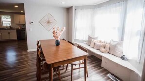 A dining area with a wooden table and chairs, a vase with flowers, and a bench with cushions by a window. - Cool, Trendy house in Dodge City! The Painted Cow (Dodge City)
