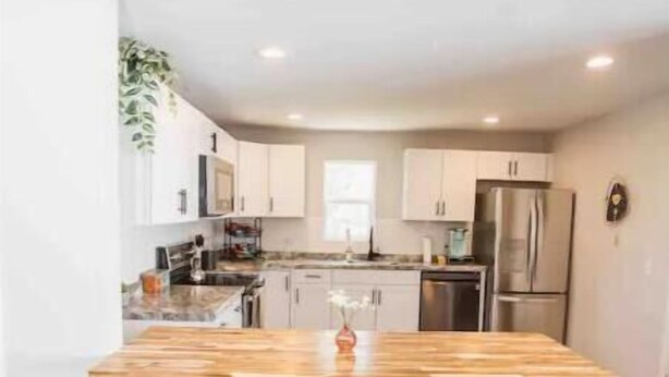 A modern kitchen with a wooden island, two bar stools, stainless steel appliances, and white cabinetry. - Cool, Trendy house in Dodge City! The Painted Cow (Dodge City)
