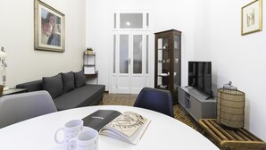 A living room with a grey sofa, a dining table with two white mugs, a book, and a television on a stand. - Italianway Easy - Ozieri 7 (Milan)