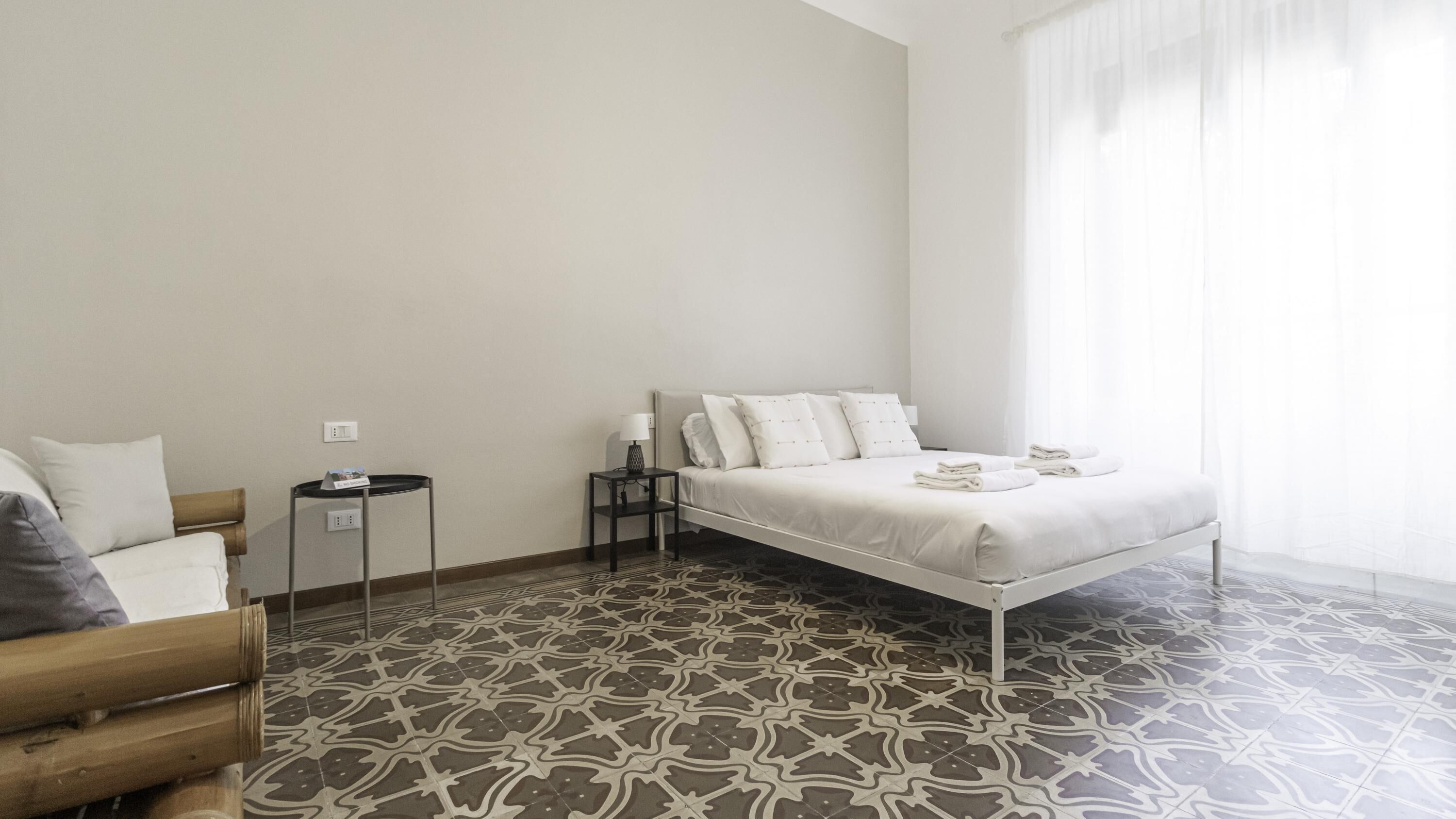 Et minimalistisk hotelværelse med seng, natbord, lampe og stol.